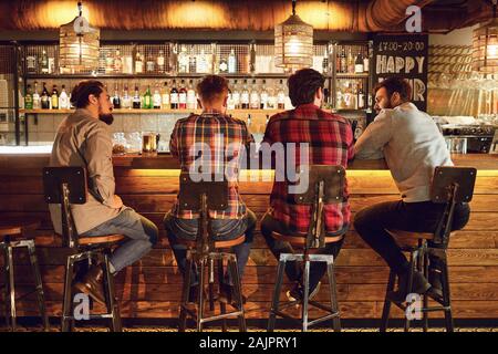 Rear view friends sitting on chairs talking at the bar in a bar. Stock Photo