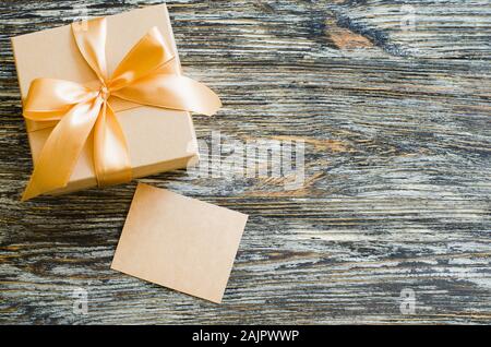 Gift craft paper box with bow ribbon and blank tag. Flat lay composition for birthday, mother day or wedding. Vintage gift box on wooden board with sp Stock Photo