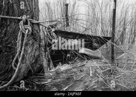 a sunken rowing boat lies on the shore of a frozen small lake