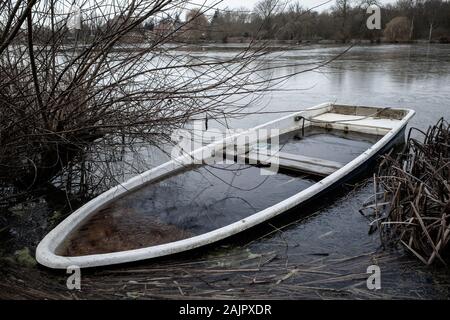 a sunken rowing boat lies on the shore of a frozen small lake