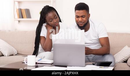 Married afro couple managing family budget at home together, reading mortgage or insurance documents, panorama with free space Stock Photo