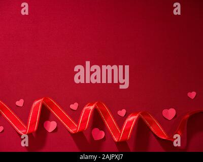Red ribbon and hearts on red fabric. Stock Photo