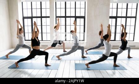 Diverse people standing in Warrior one pose, practicing yoga Stock Photo