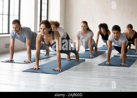 Diverse people with trainer practicing yoga, doing Plank exercise Stock Photo