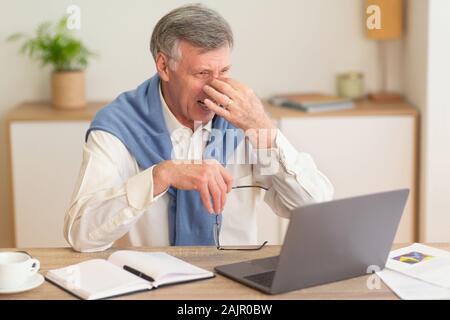 Eyestrain Concept. Elderly Businessman At Laptop Massaging Nosebridge Having Headache Or Sore Eyes Sitting In Modern Office. Selective Focus Stock Photo