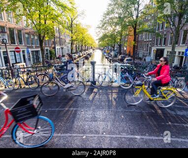 Bicycle riders are passing a canal bridge in Amsterdam's old Jordaan quarter (Egelantiersgracht) Stock Photo