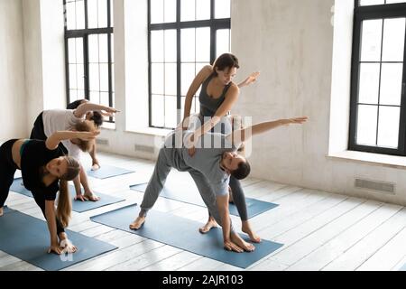 Instructor helping man at yoga lesson, doing extended triangle exercise Stock Photo