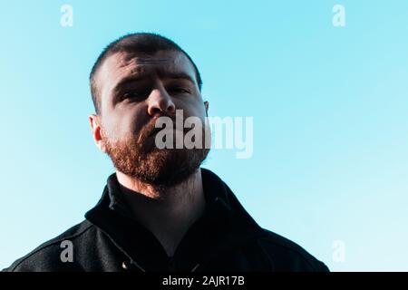Sad depressed face of a short haired balding bearded man looking straight at the camera in defeat. Dark harsh shadows on mans face Stock Photo