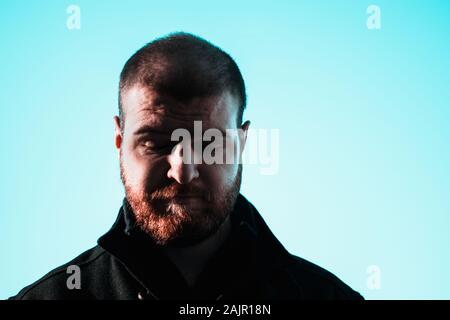 Sad depressed face of a short haired balding bearded man looking down at the floor. Eyes closed in defeat. Dark harsh shadows on mans face Stock Photo