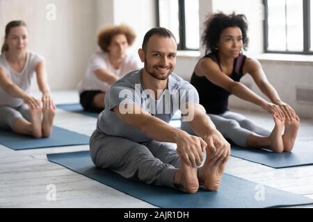 Smiling man practicing yoga at group lesson, Seated forward bend Stock Photo