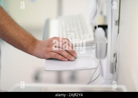 The doctor's hand on a computer mouse near the computer keyboard in the operating room Stock Photo