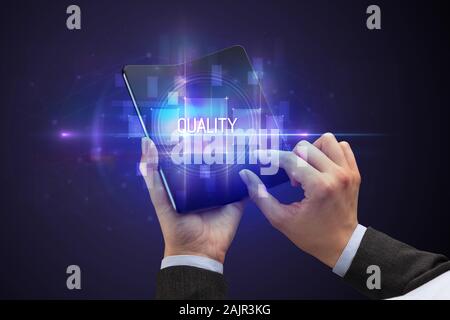 Businessman holding a foldable smartphone with QUALITY inscription, new technology concept