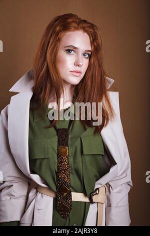 Fashion. Beautiful woman in autumn jacket, trendy hairstyle, make up. Adorable well dressed ginger girl on brown nackground. Gorgeous fashionable lady Stock Photo