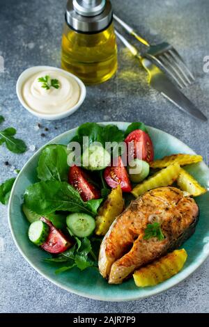 Vegetarian lunch or dinner, healthy eating concept. Grilled salmon, rustic baked potatoes and salad with fresh vegetables on a stone countertop. Stock Photo