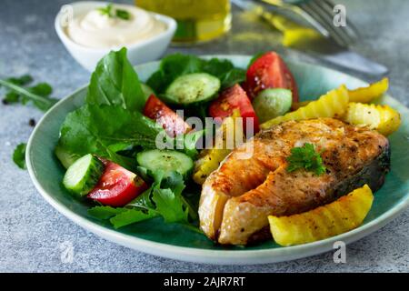 Vegetarian lunch or dinner, healthy eating concept. Grilled salmon, rustic baked potatoes and salad with fresh vegetables close-up on a stone countert Stock Photo