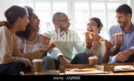 Overjoyed multiethnic millennial friends eating pizza at home Stock Photo
