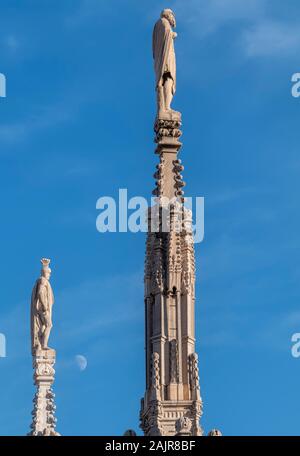 Milan Italy. Statues on the spires of the Duomo cathedral and moon Stock Photo