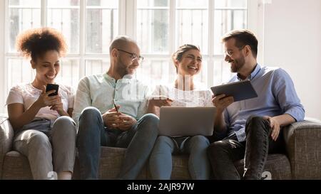 Happy young people sit on couch using modern electronic devices Stock Photo