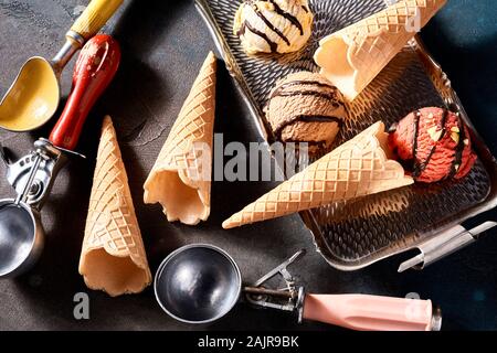 Ice cream still life with wafer cones and scoops viewed from overhead with three flavors of dessert on a small tray for serving