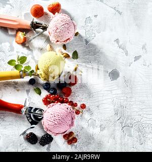 Three metal scoops of berry and nut ice cream with mixed berry, strawberry and pistachio nut flavors on an old wood background with cracked white pain Stock Photo