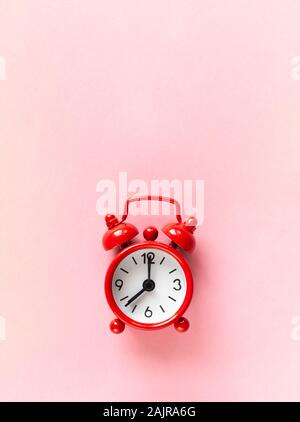 Red small alarm clock on pastel pink background with copy space, flat lay, macro. Minimalism style. Time management, countdown concept. Vertical orien Stock Photo