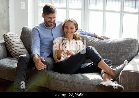 Happy millennial couple relax on couch using cellphone Stock Photo