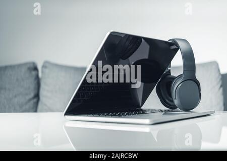 Computer Online Music Listening. Modern Laptop and Headphones on Elegant White Glassy Table. Technology Theme. Stock Photo