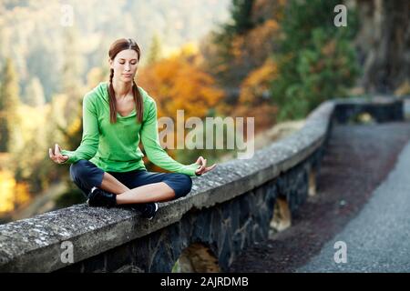 Woman meditating on rock wall on side of the road Stock Photo