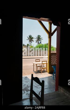 Table and chairs in the terrace of a bar close to road and palm trees in Morondava, Madagascar Stock Photo