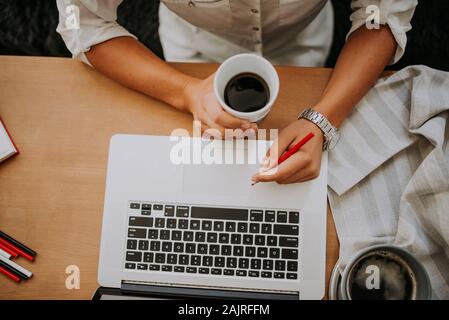 Young businesswoman drinking coffee and working on laptop in her Stock Photo