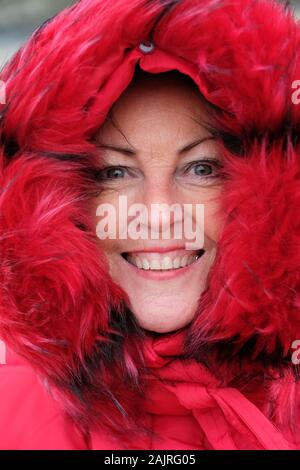 Close-up of a mature, beautiful woman in a red, fur-lined parka - John Gollop Stock Photo