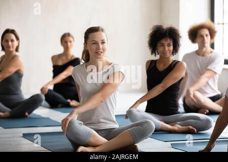 Young diverse people practicing yoga, sitting in Parivritta Sukhasana pose Stock Photo