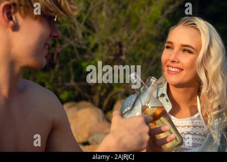 Smiling Young Couple Toasting Beer Bottles At Beach Stock Photo