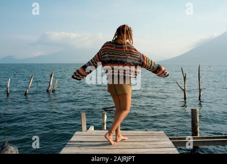 Rear view of attractive Caucasian woman dancing on a jetty. Outdoor lifestyle, solo travel, holiday, recreational concept. Lake Atitlán, Guatemala Stock Photo