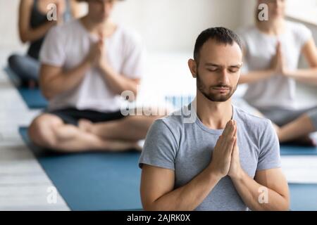 Young man meditating at group lesson close up, practicing yoga Stock Photo