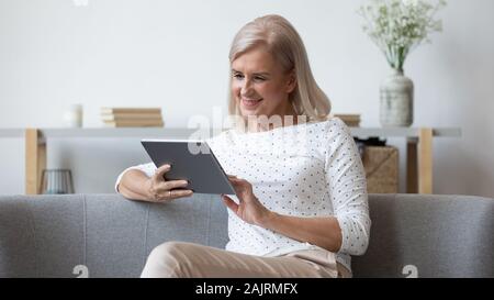 Modern elderly woman using tablet relaxing at home Stock Photo