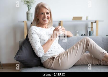 Portrait of smiling mature woman relaxing on couch with cup Stock Photo
