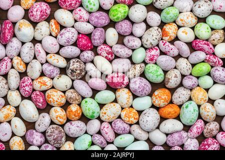 Mix of sweets in the form of multi-colored spotted pebbles on a brown wooden background. A high resolution. Stock Photo