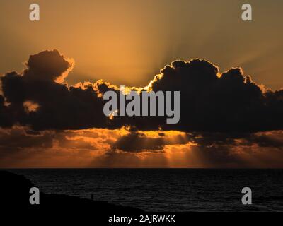 Sunset on the beach with the sun behind the clouds Stock Photo