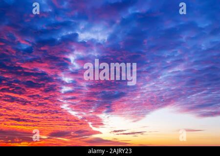 Sunset fire in the sky. Dark blue clouds with red reflections of the setting sun. Scenic sundown cloudscape for background. Dramatic cloudscape. Stock Photo