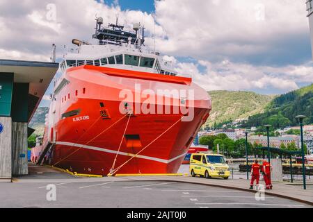 Two Norwegian paramedics in red uniforms are resting near an ambulance parked in a port near a large ship. Theme healthcare and medicine in Norway Stock Photo