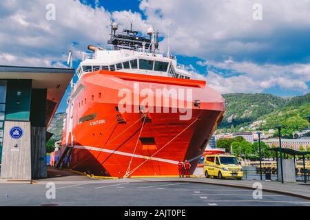 Two Norwegian paramedics in red uniforms are resting near an ambulance parked in a port near a large ship. Theme healthcare and medicine in Norway Stock Photo