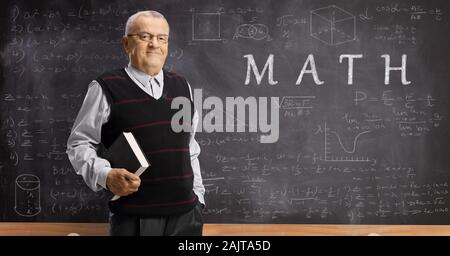 Mature math teacher with a book in front of a blackboard with formulas and text math Stock Photo