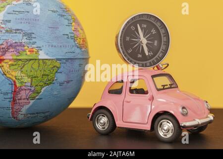 Pink retro car and compass with world globe sphere on yellow background, close-up toned photo Stock Photo