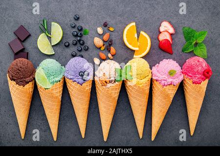 Various of ice cream flavor in cones blueberry ,lime ,pistachio ,almond ,orange ,chocolate ,vanilla and coffee set up on dark stone background . Summe Stock Photo