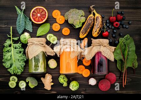 Colourful healthy smoothies and juices in bottles with fresh tropical fruit and superfoods on wooden background. Stock Photo
