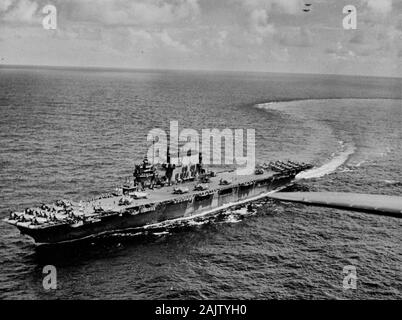 The U.S. Navy aircraft carrier USS Saratoga (CV-3) in 1943/44. The photo was taken from one of her planes of Carrier Air Group 12 (CVG-12), of which many aircraft are visible on deck, Douglas SBD Dauntless dive bombers (aft), Grumman F6F Hellcat fighters (mostly forward), and Grumman TBF Avenger torpedo bombers. Stock Photo