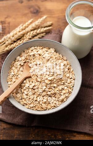 Oatmeal, oat flakes, rolled oats and vegan oat milk in bottle on a wooden table. Healthy breakfast food, clean eating, dieting concept Stock Photo