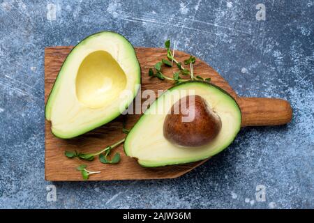 Halved avocado on a chopping board on blue background. Top view. Healthy vegan vegetarian food Stock Photo