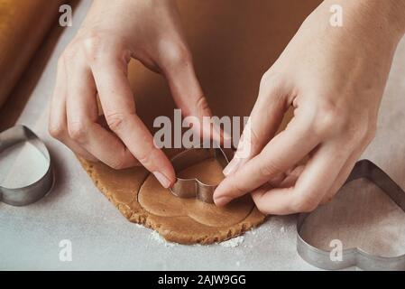 Making gingerbread cookies in shape of a heart for Valentines Day. Woman hand use cookie cutter. Holiday food concept Stock Photo
